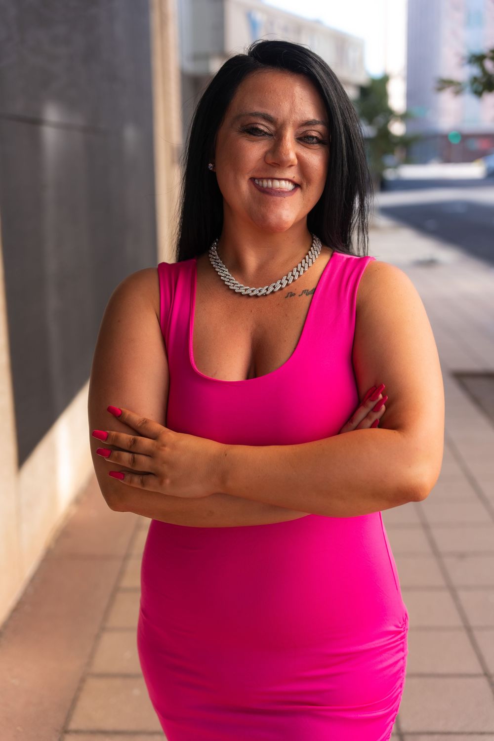 Person in bright pink tank top poses confidently against urban backdrop.