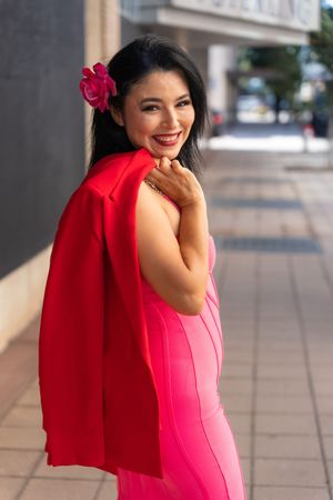 Model in vibrant pink outfit poses expressively against city background.