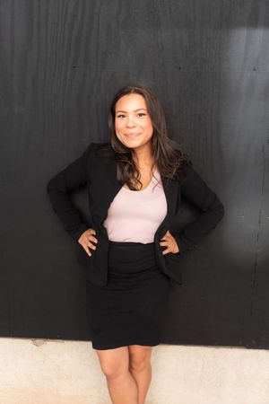 Model in black blazer and pink top poses against dark background.