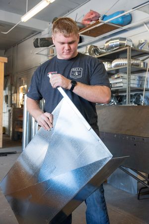 Worker in navy shirt demonstrates metal fabrication techniques in workshop.
