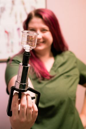 Therapist demonstrates glass cupping tools against pink background in professional setting.