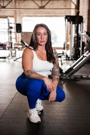 Athletic figure in blue workout gear and white sneakers poses in industrial gym setting.