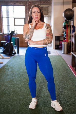 Person wearing bright blue leggings demonstrates fitness poses on green gym flooring.