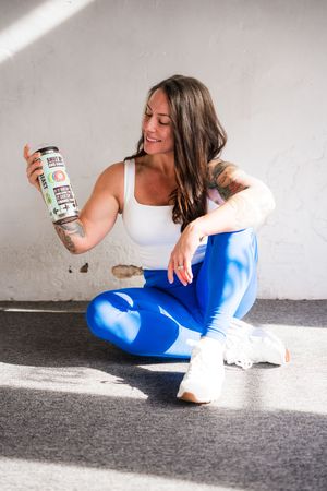 Individual in white top and blue pants relaxes on floor with snacks in natural lighting.