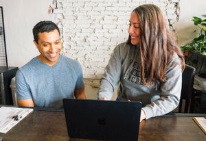 People working together at desk with laptops against white brick wall background.