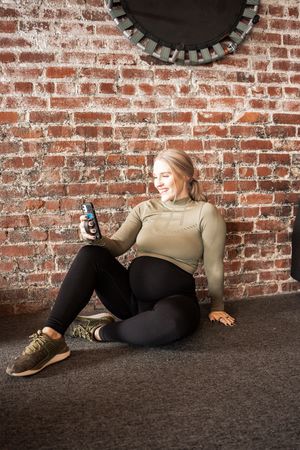 Person in beige sweater relaxing against rustic brick wall in casual poses.