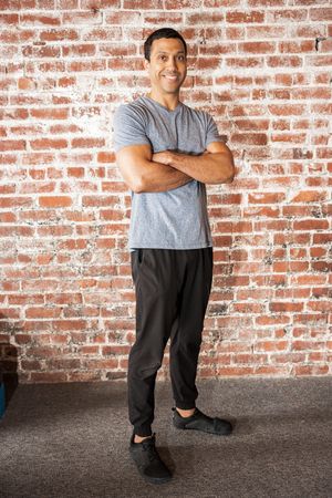 Person in grey t-shirt poses casually against brick wall background.