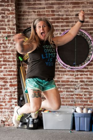 Person in green shorts jumping energetically in front of brick wall during workout session.
