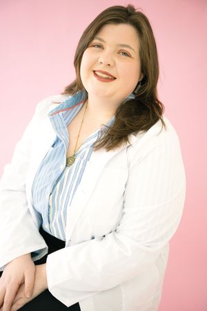 Person in white blazer and striped shirt poses against pink backdrop with warm expressions.