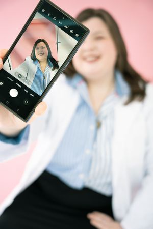 Smartphone capturing portrait photos against pink background.