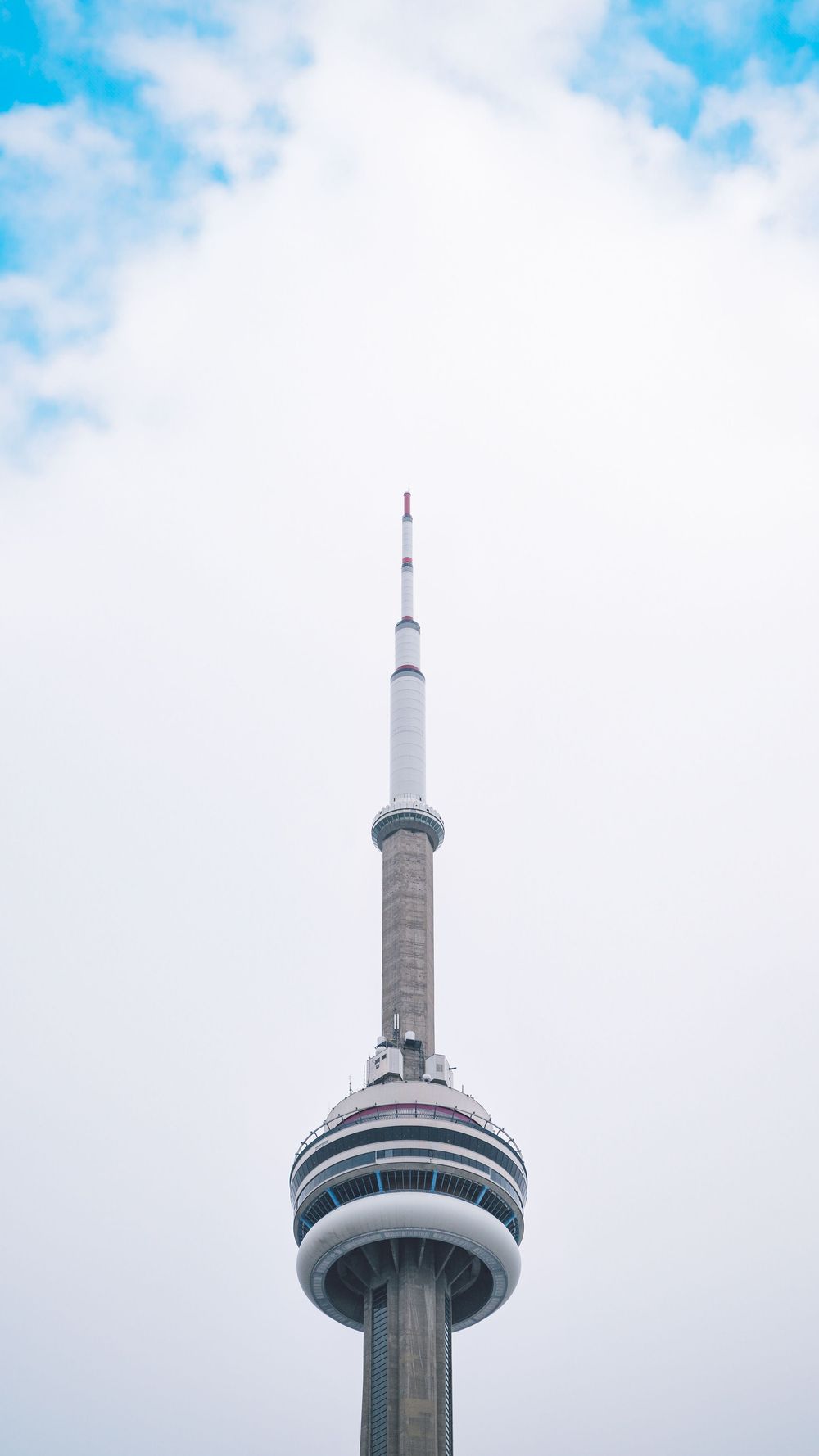 The CN Tower in Toronto rises into a cloudy sky, showing multiple views of its iconic observation deck and spire.