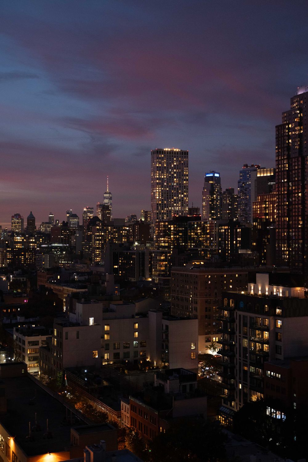 Panoramic view of New York City skyline at dusk with illuminated skyscrapers against a dramatic purple and blue sky.