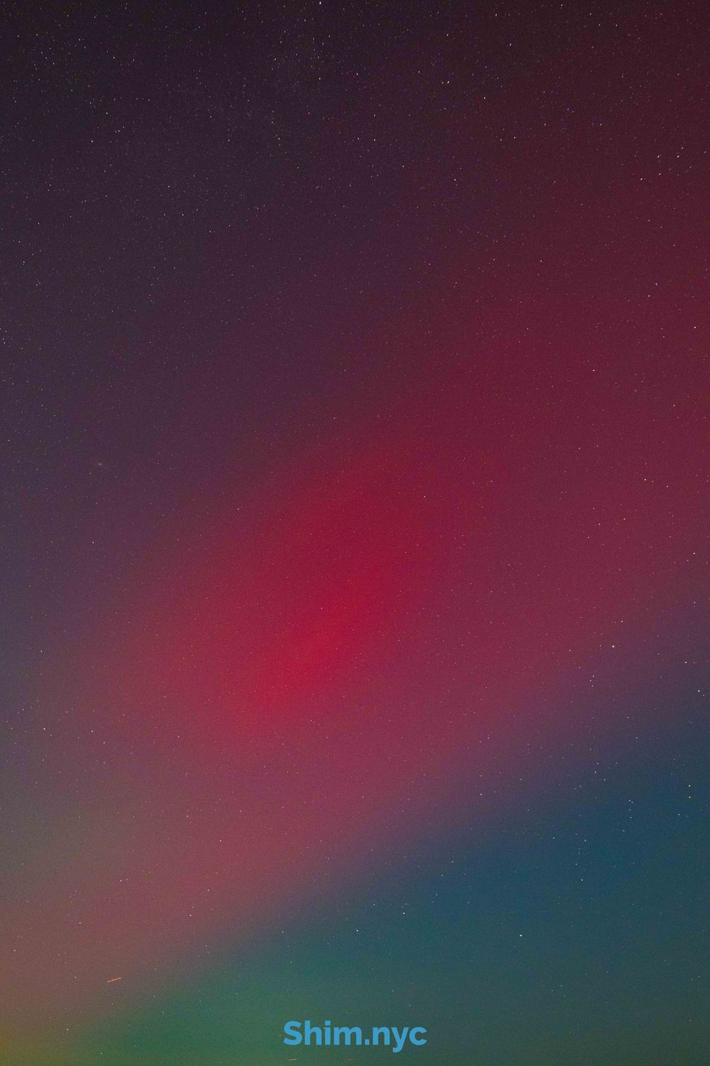 A dark atmospheric photo showing a gradient of deep purple to red and teal colors in the night sky.