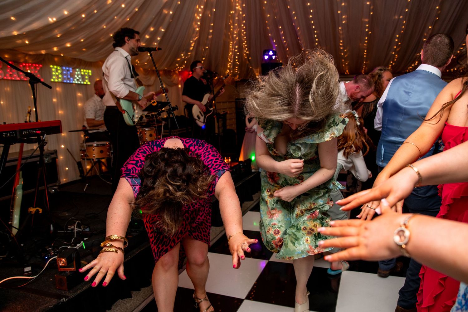 Wedding guests dancing and celebrating under string lights in a festively decorated reception venue.