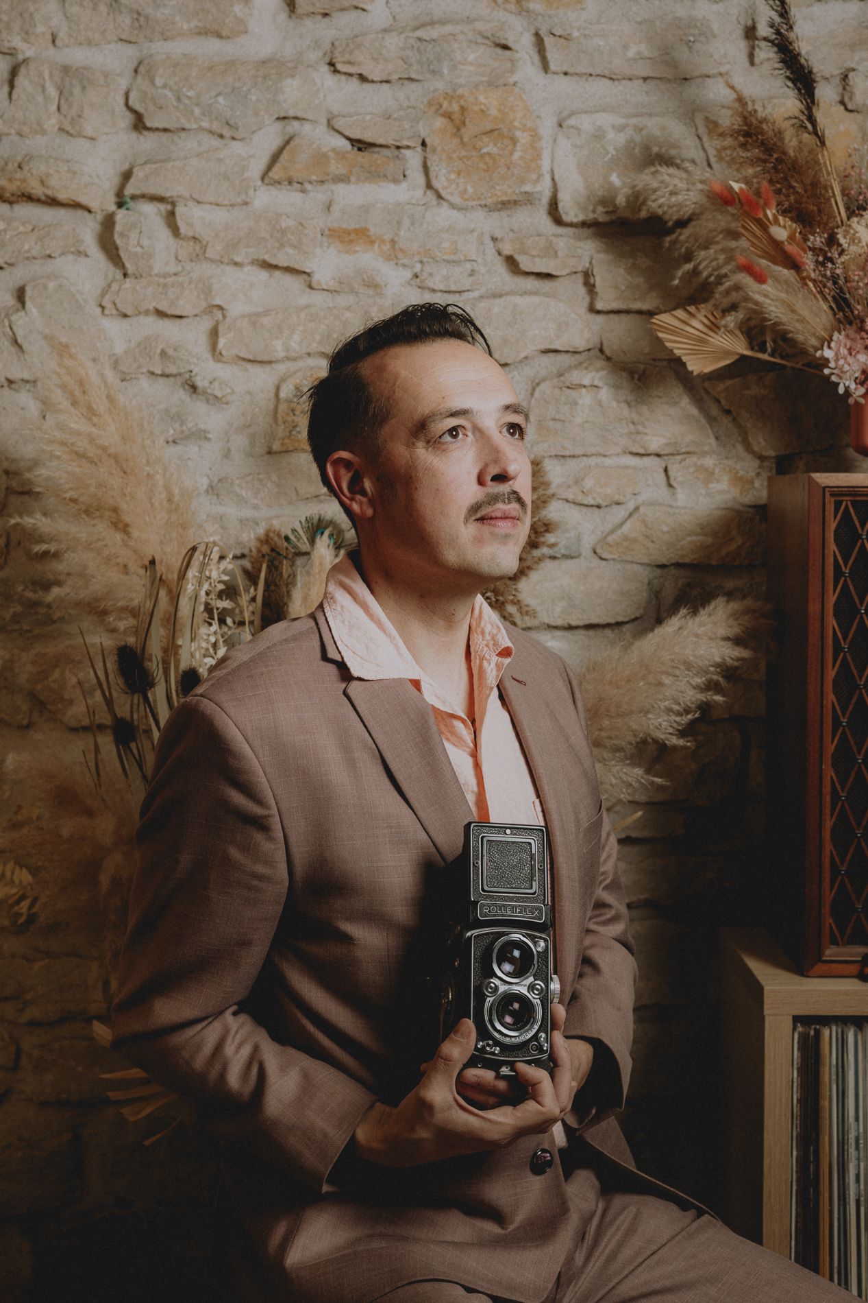portrait of a French wedding photographer in a pastel pink costume holding a vintage camera and looking away