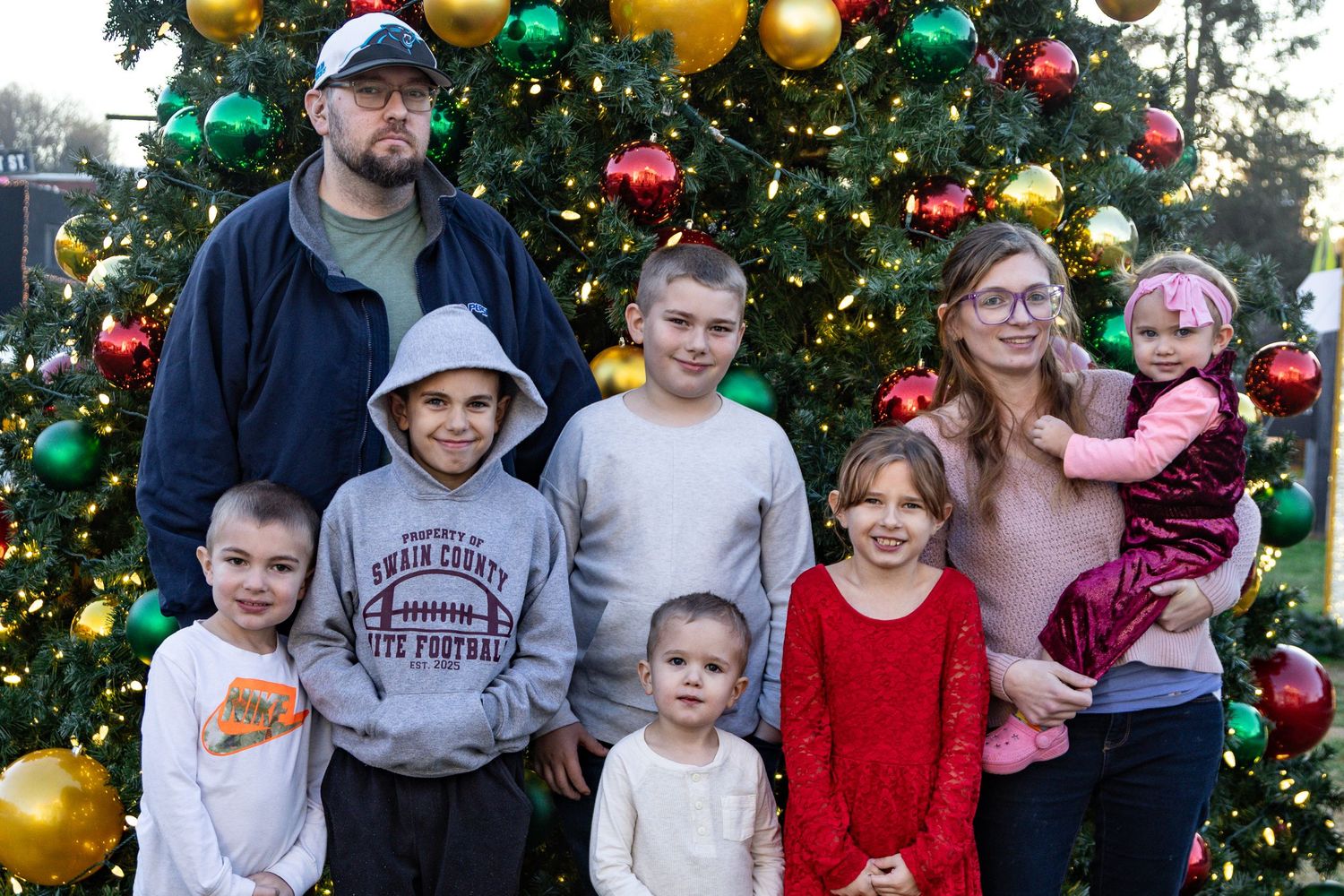 Group photo of children and adults sitting together on blanket during outdoor family photoshoot.