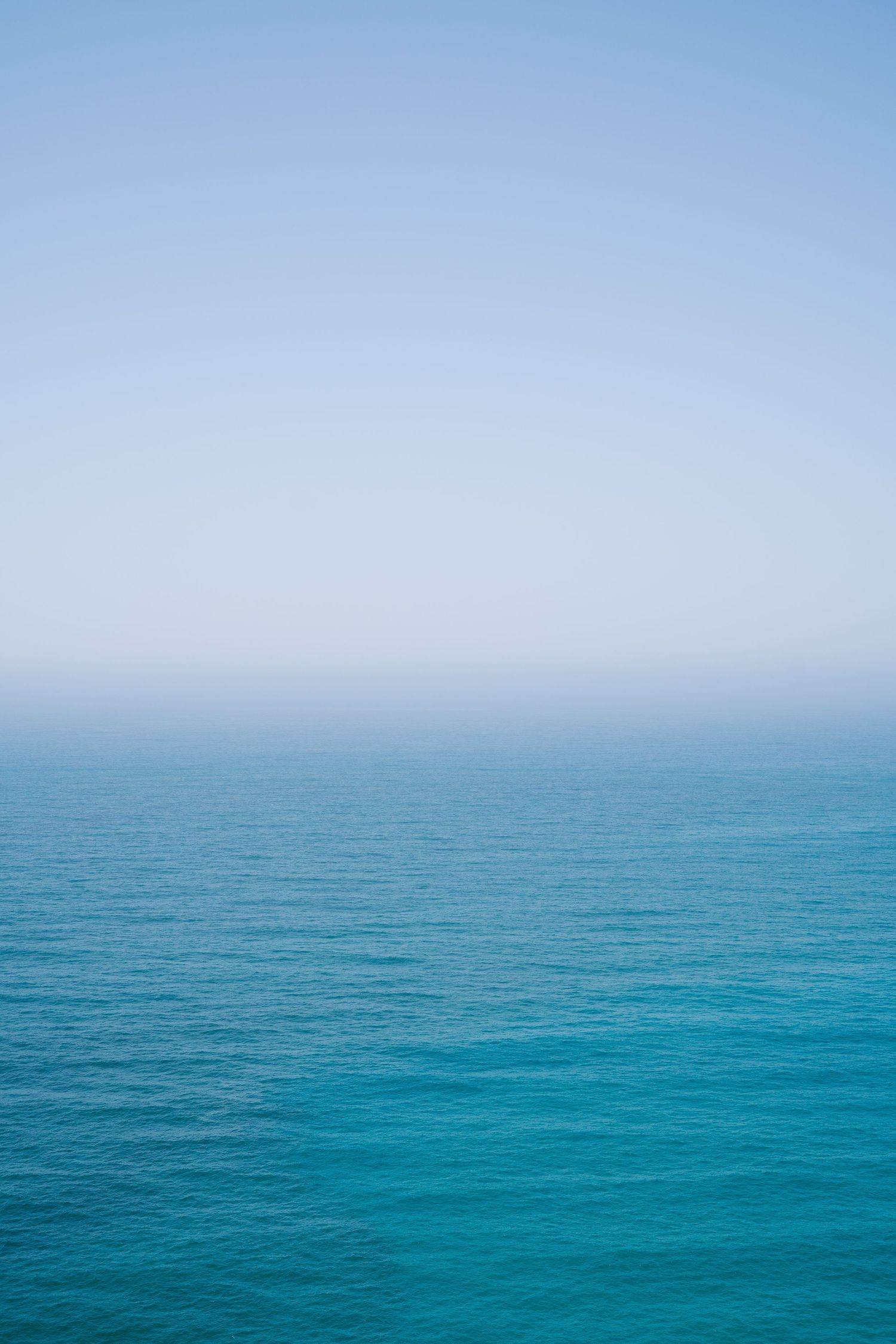 Minimalist seascape showing calm turquoise ocean meeting clear blue sky on the horizon.