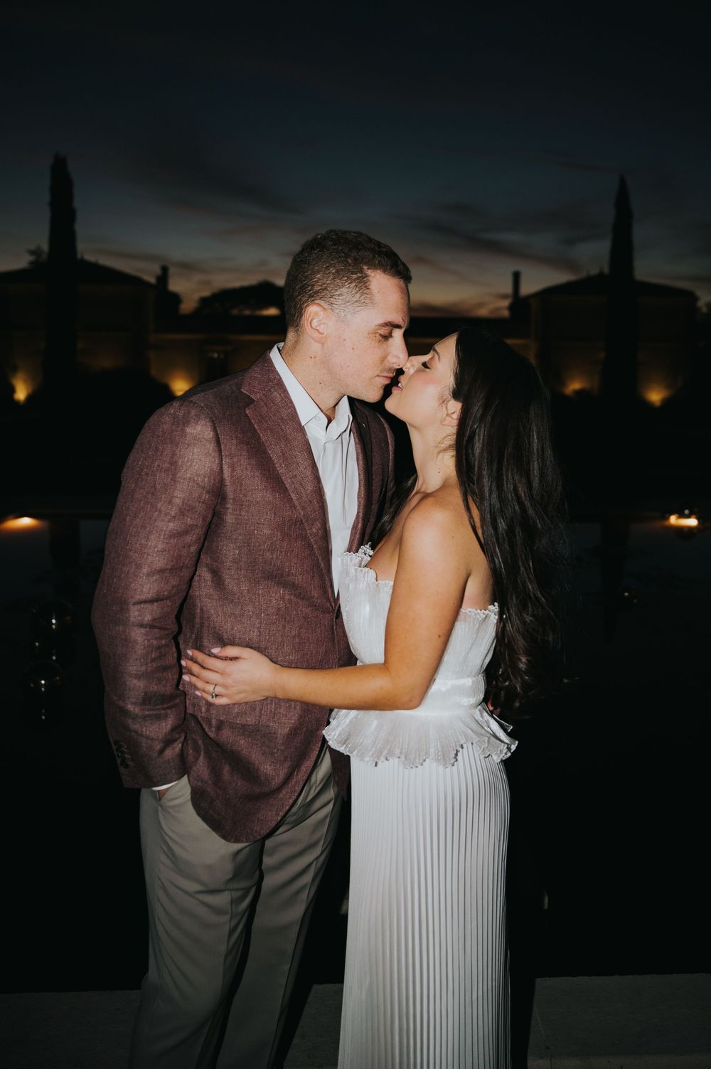 A romantic couple shares a tender moment at sunset against a darkening city skyline.