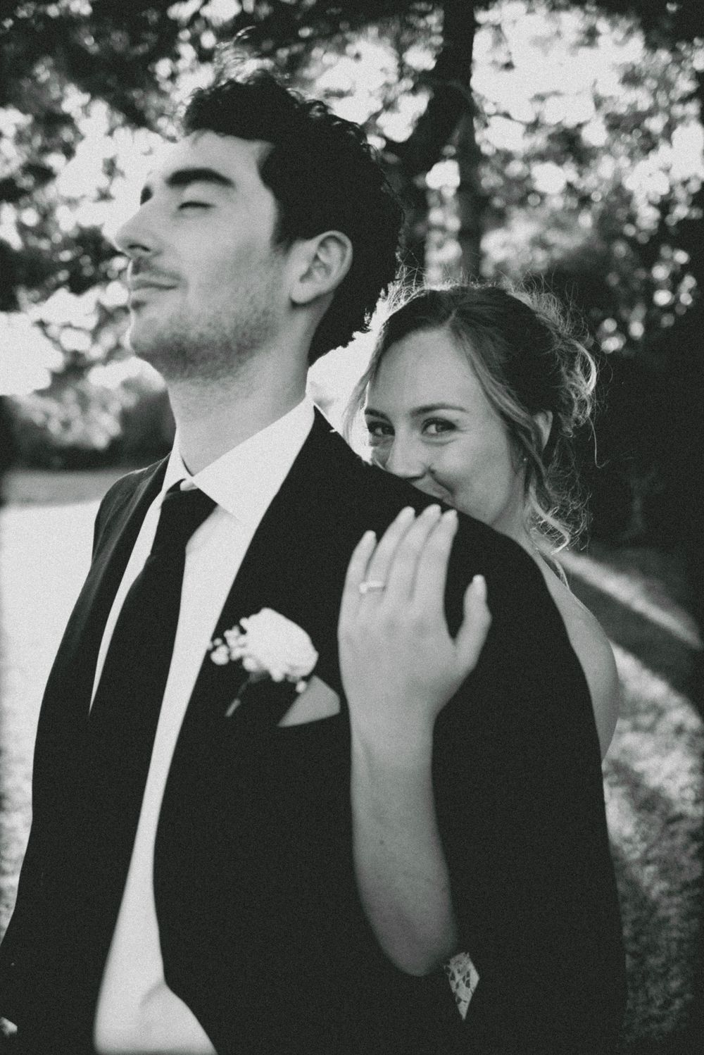 A black and white candid wedding photo showing a joyful couple posing together outdoors in formal attire.