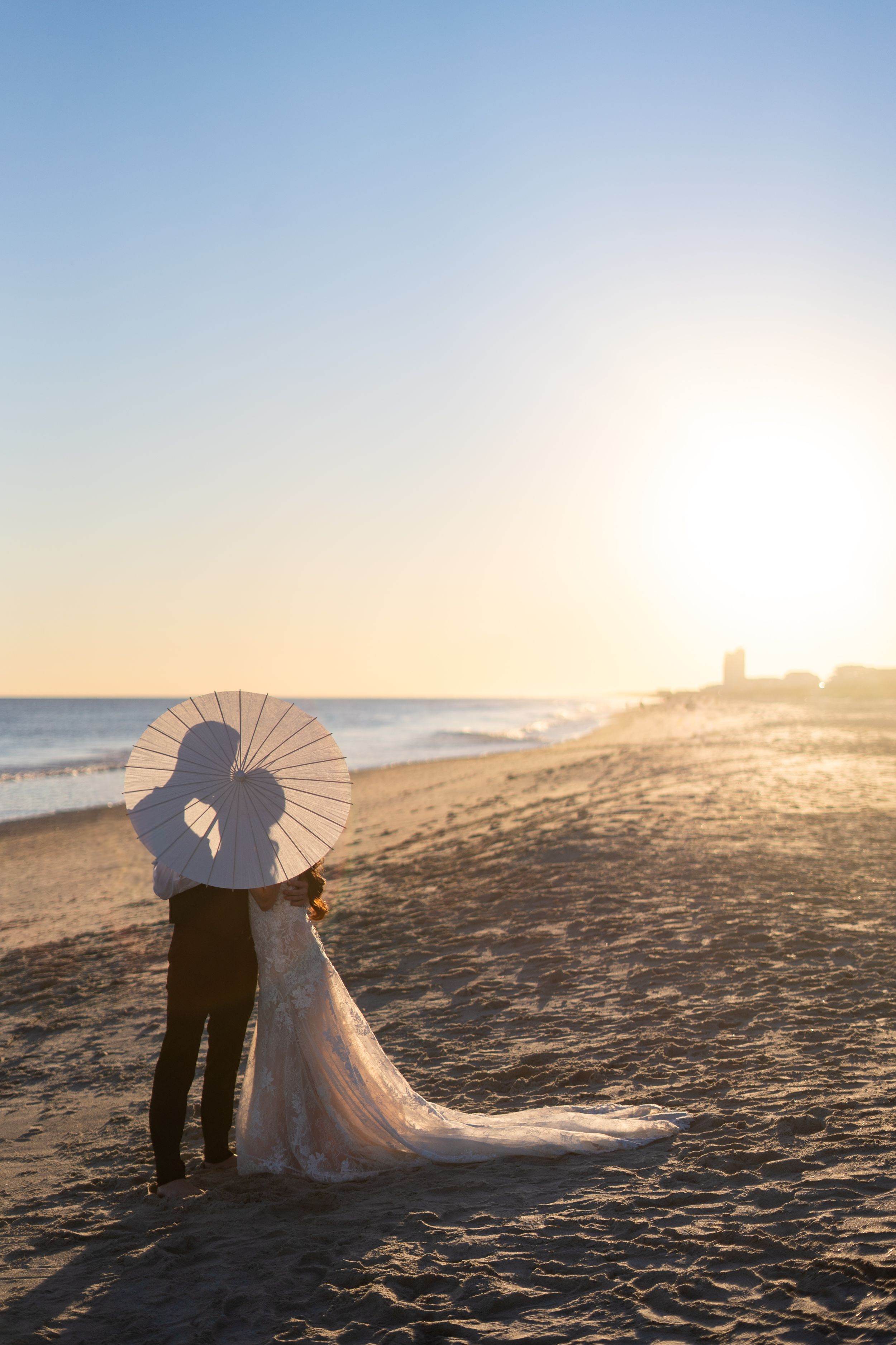 Romantic beach silhouette of couple with parasol during sunset wedding photo.