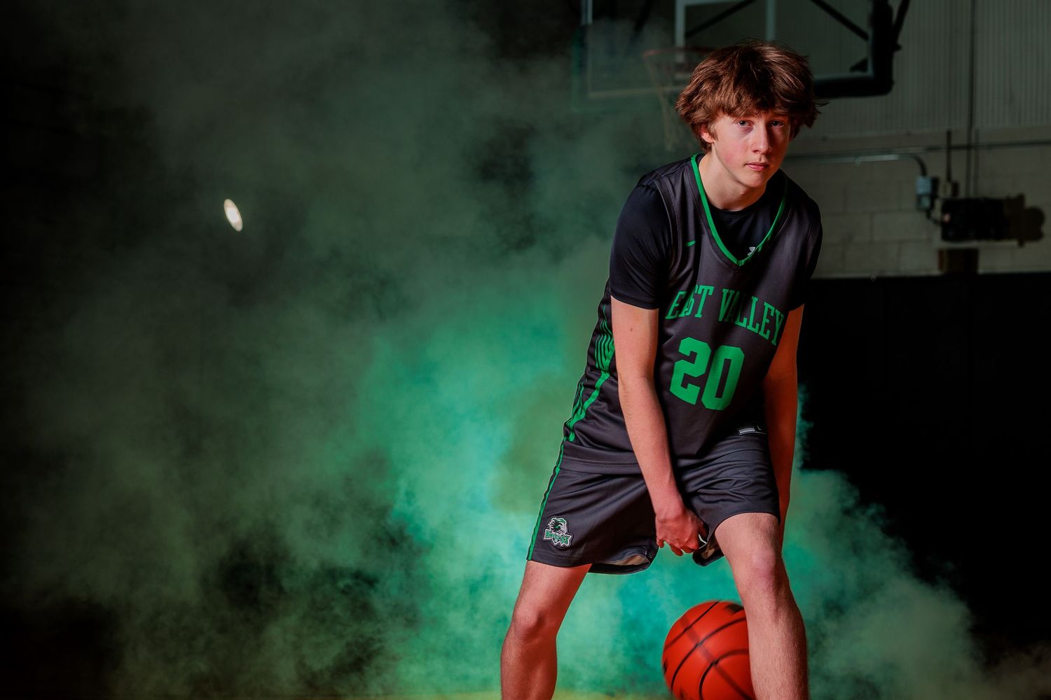 A young high school female athlete in a uniform confidently holds a basketball, showcasing her athleticism and passion for the sport.