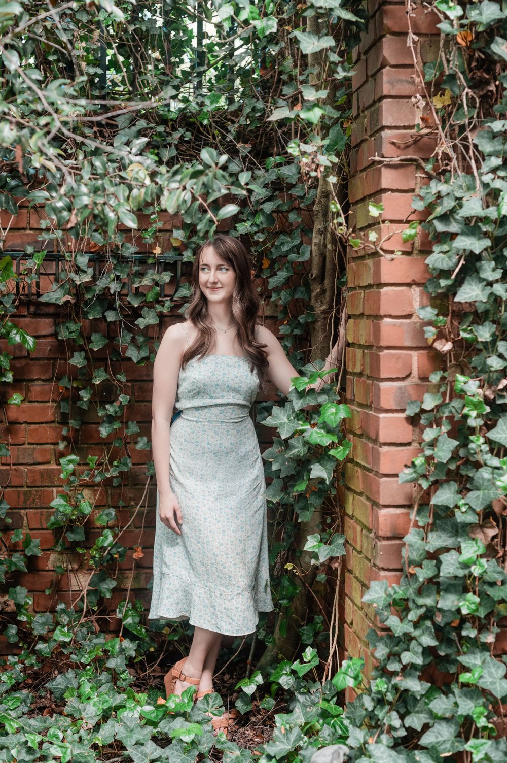 Outdoor senior portrait of a high school graduate girl, in a garden with ivy and brick walls.
