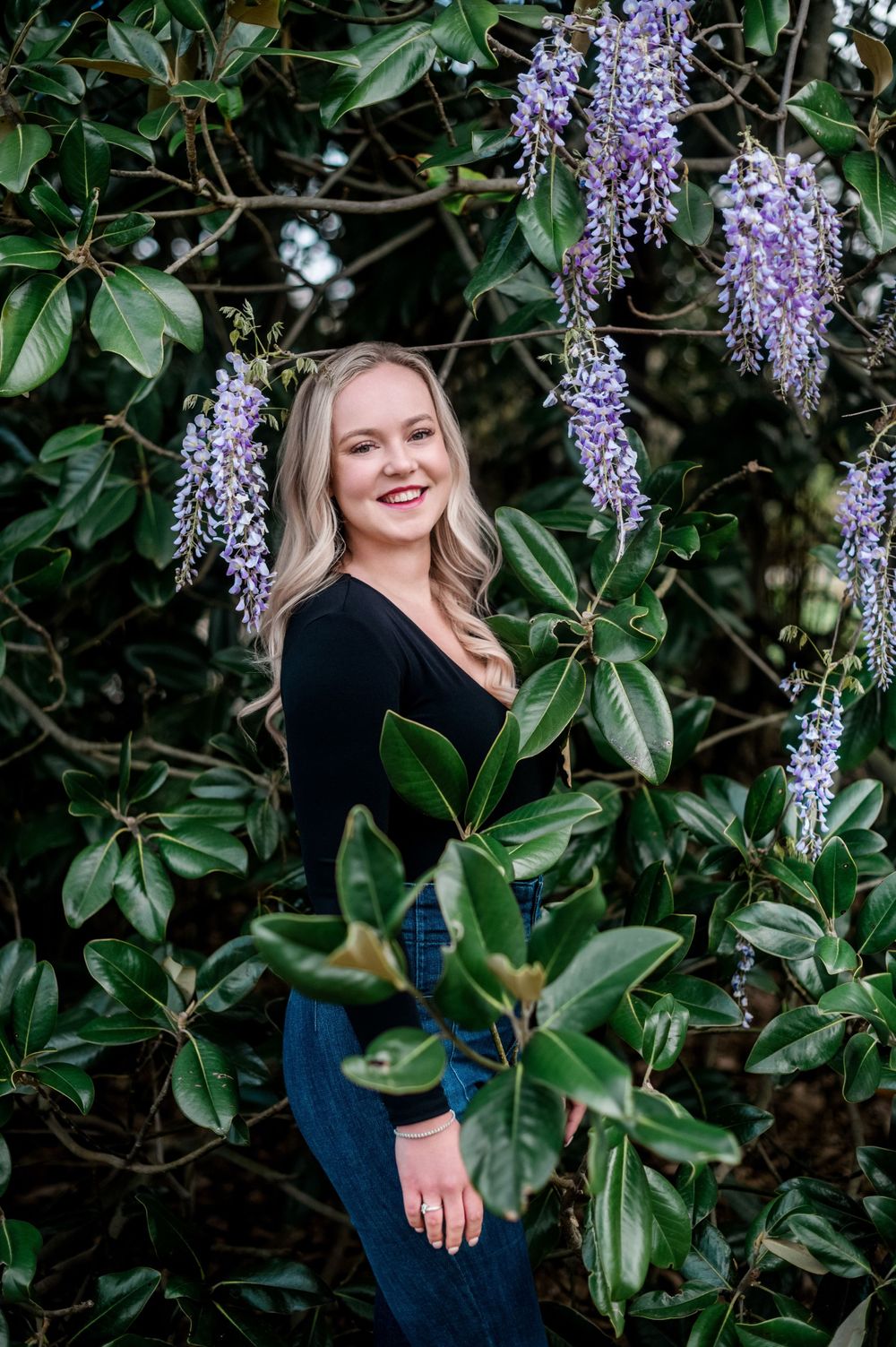 Stylized college senior portrait session, featuring creative poses and vibrant background of wisteria.