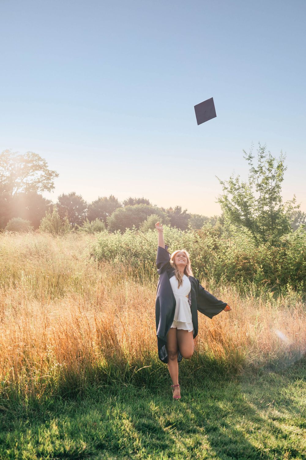 High school senior girl photo session at a golden field, throwing her cabin the air with joy.