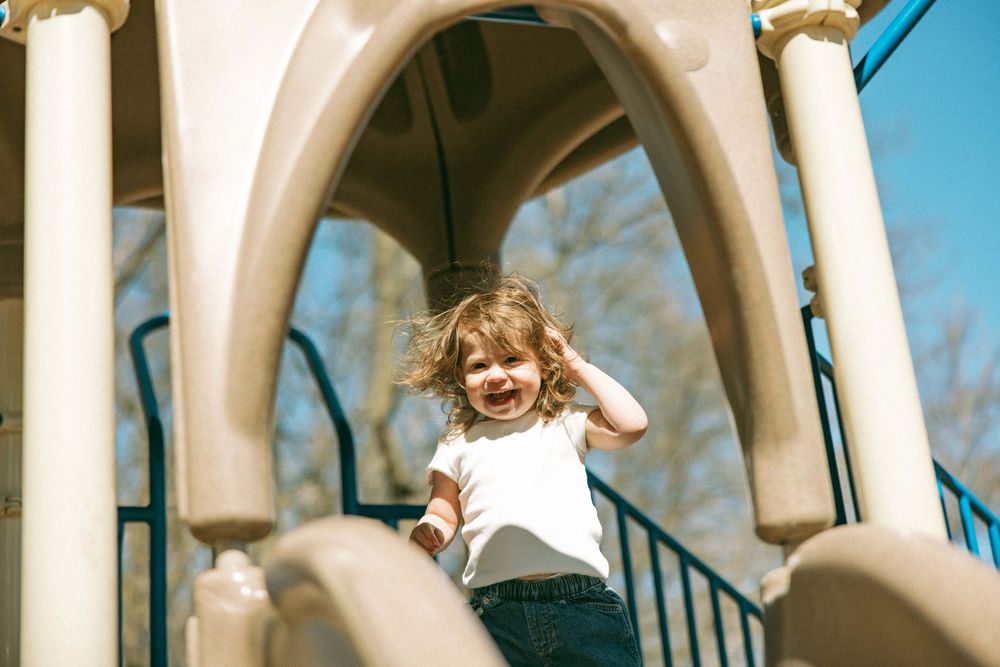 Happy toddler girl playing on a playground structure on a sunny day.