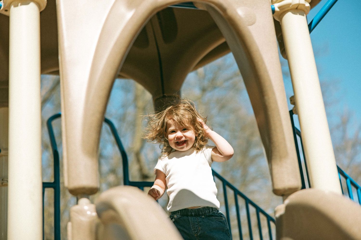 Happy toddler girl playing on a playground structure on a sunny day.