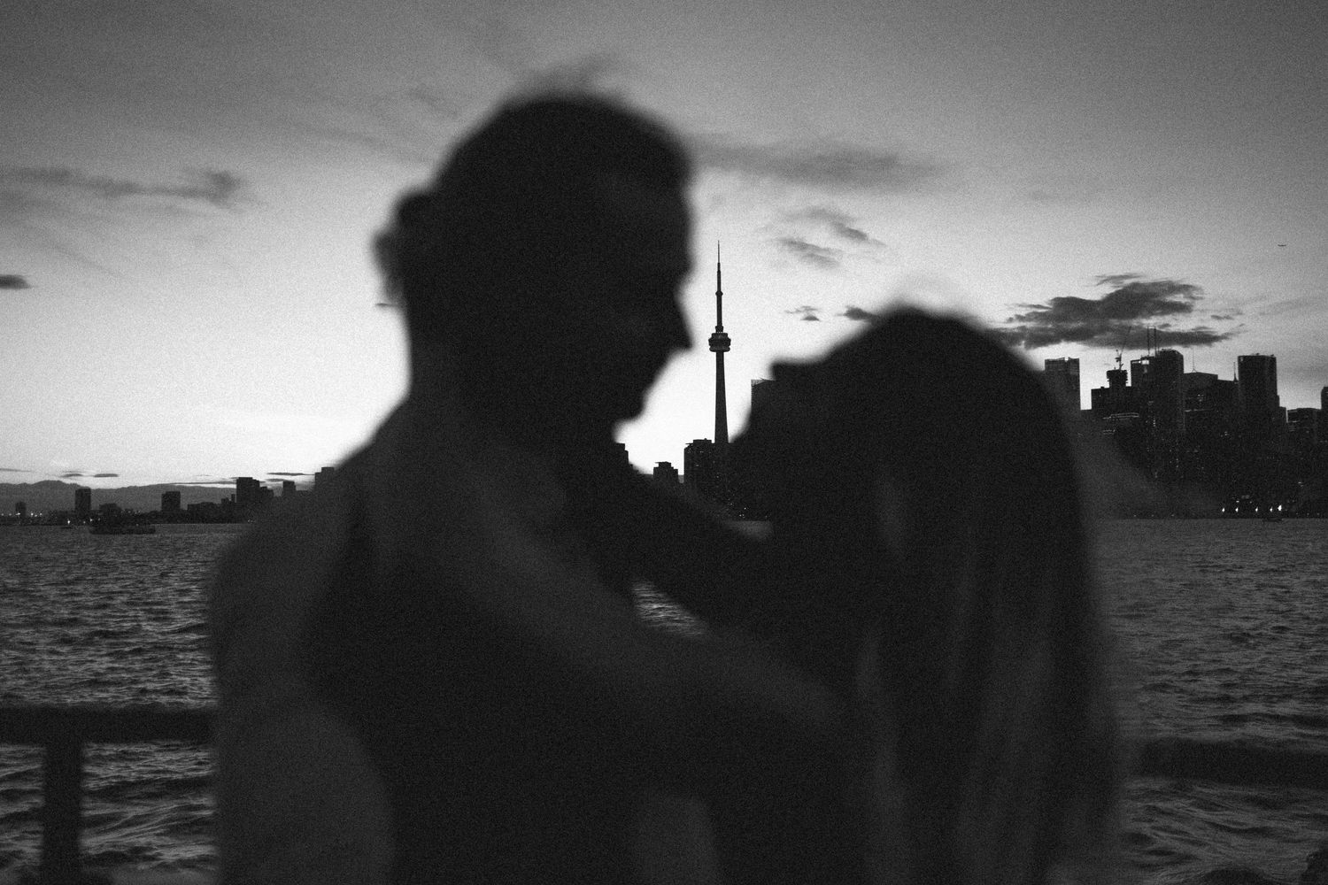 Silhouettes of a couple against a sunset skyline with a prominent cn tower in the background. Toronto