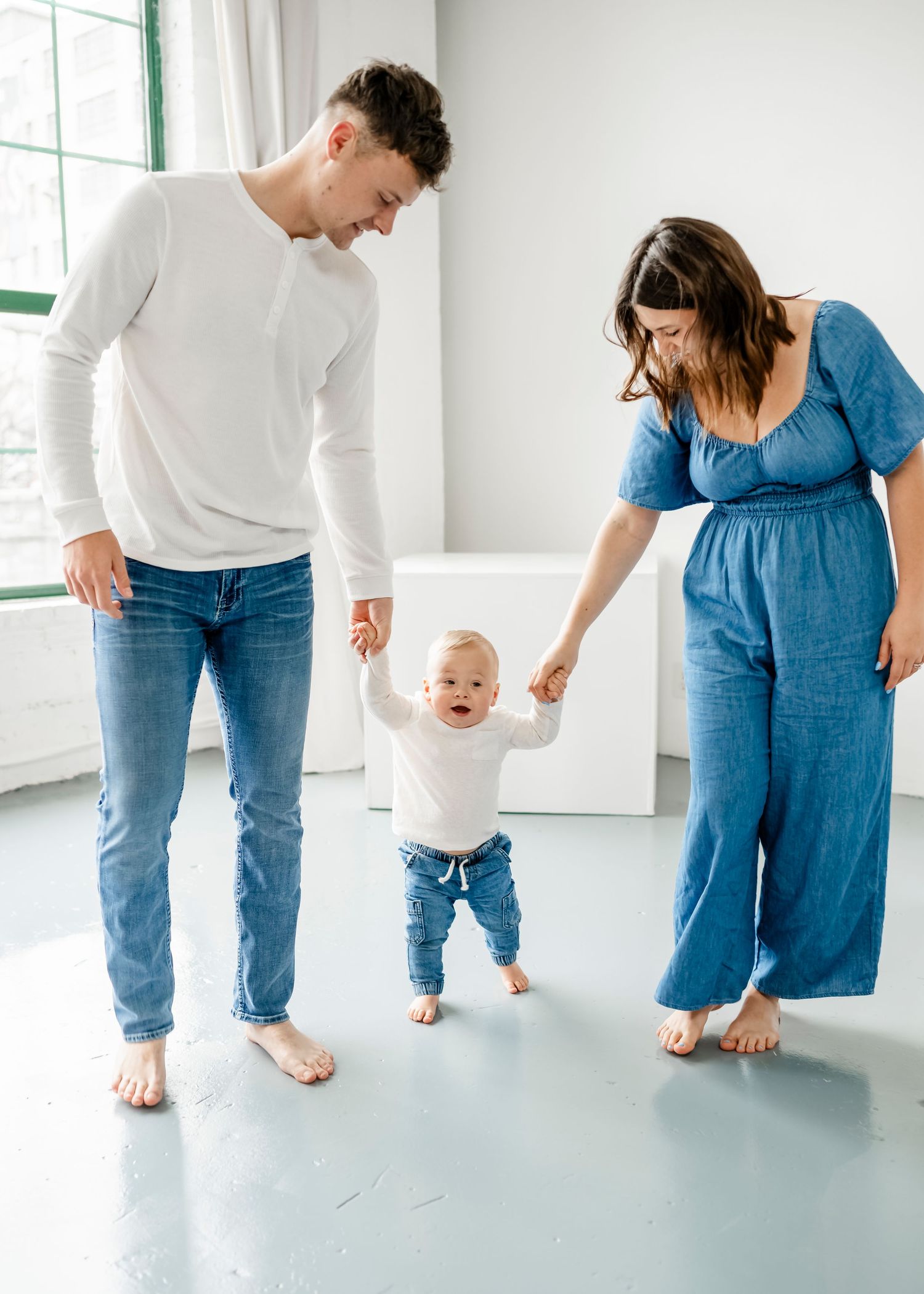 Parents help their baby take first steps in a bright minimalist room.