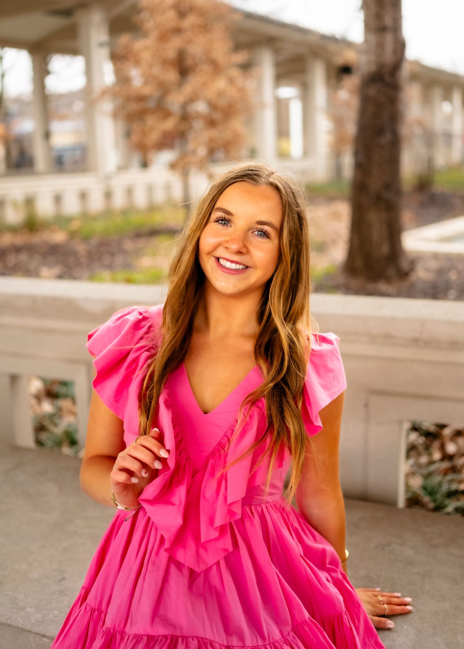 A vibrant hot pink dress with ruffled details shown against an outdoor urban backdrop.