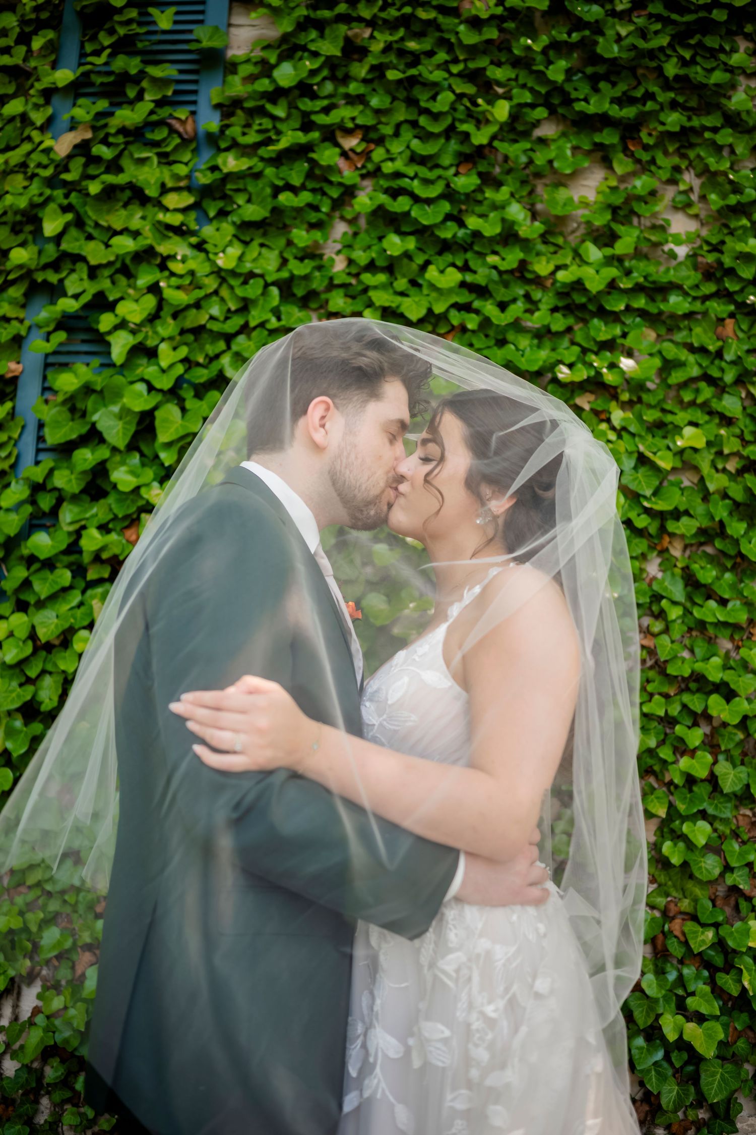 Intimate wedding moment captured against lush green ivy backdrop with flowing veil.