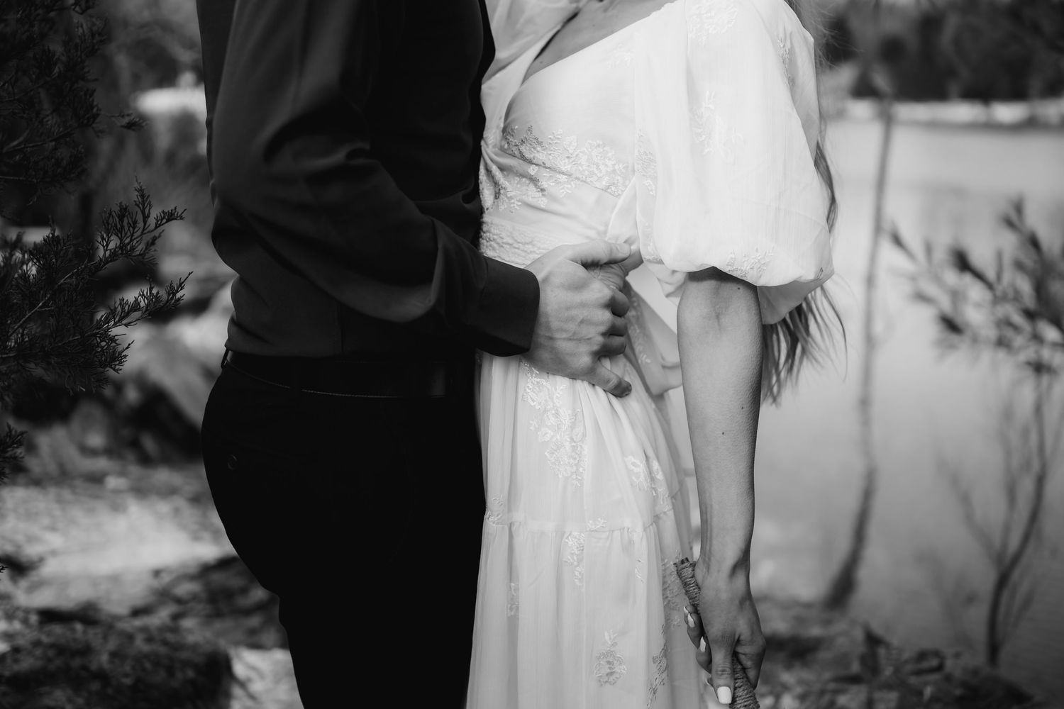A romantic black and white photo of a couple embracing outdoors.