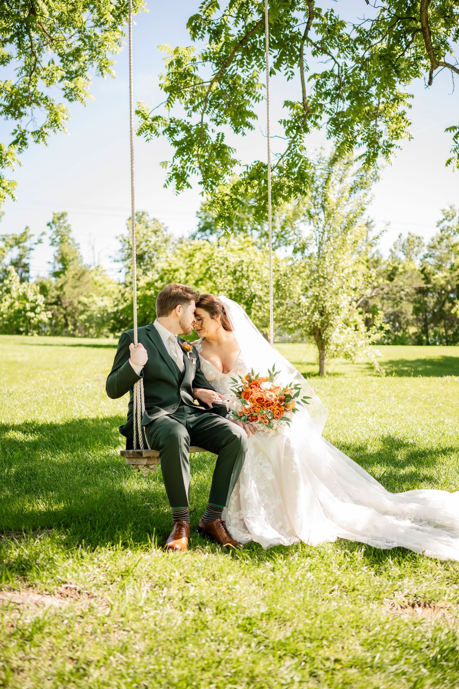Romantic wedding couple poses in sunny meadow with flowing white dress and colorful bouquet.