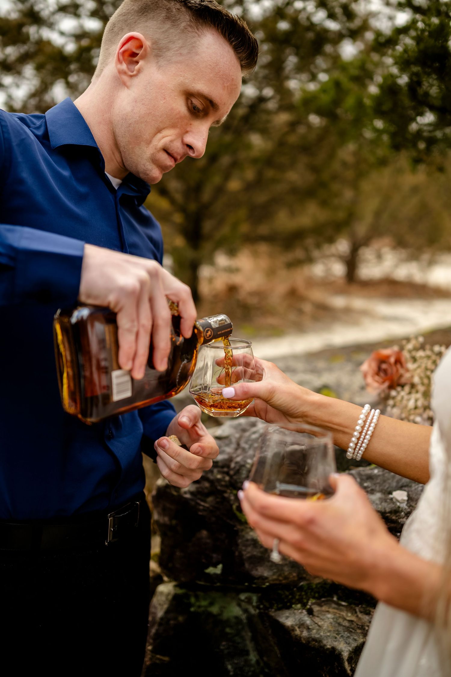 Close-up shots of hands opening a bottle in an outdoor setting.