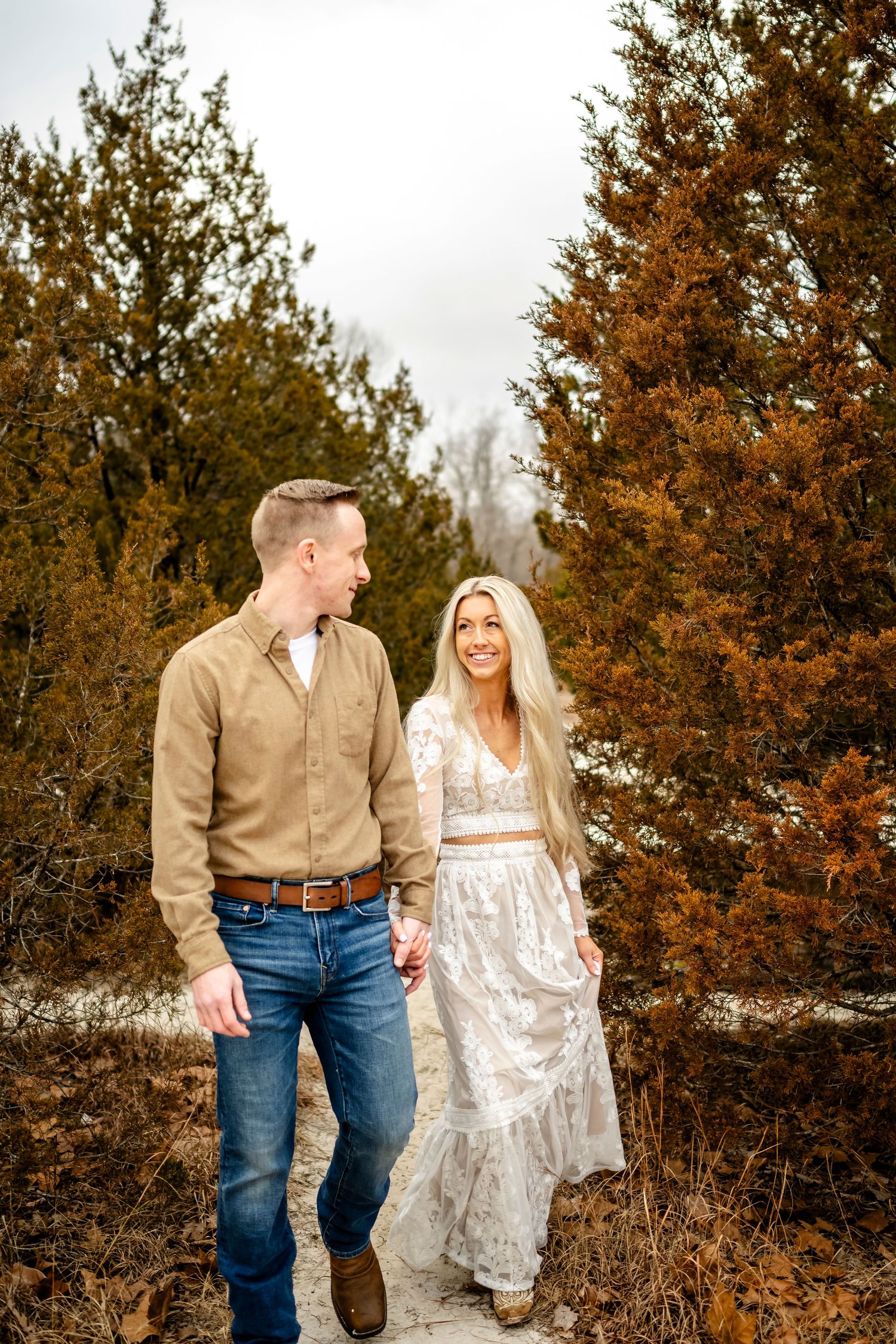 A couple walking through autumn foliage in casual western attire.