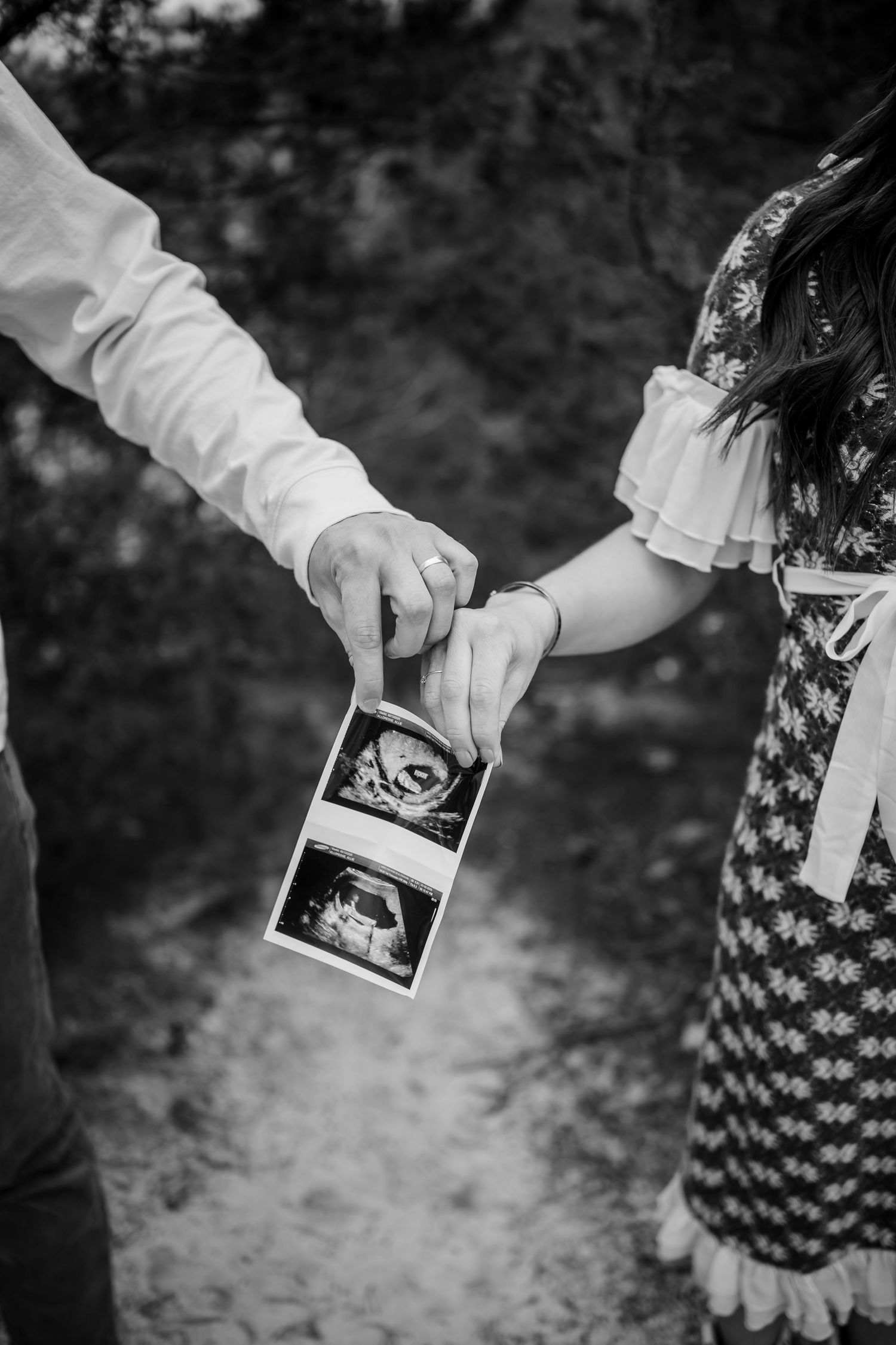 Hands holding ultrasound photos in black and white outdoor setting.