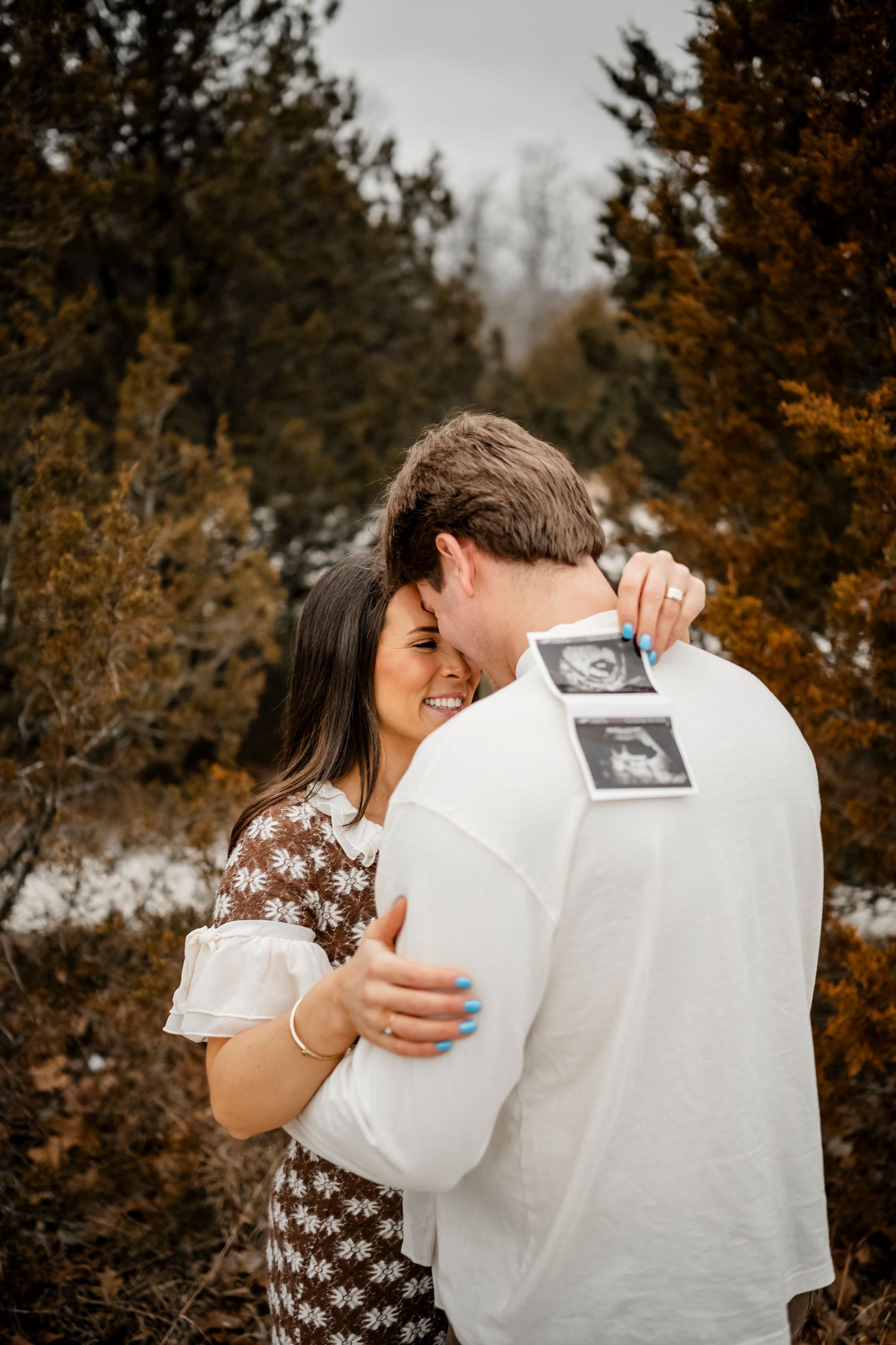 Intimate pregnancy announcement moment captured in autumn forest setting.