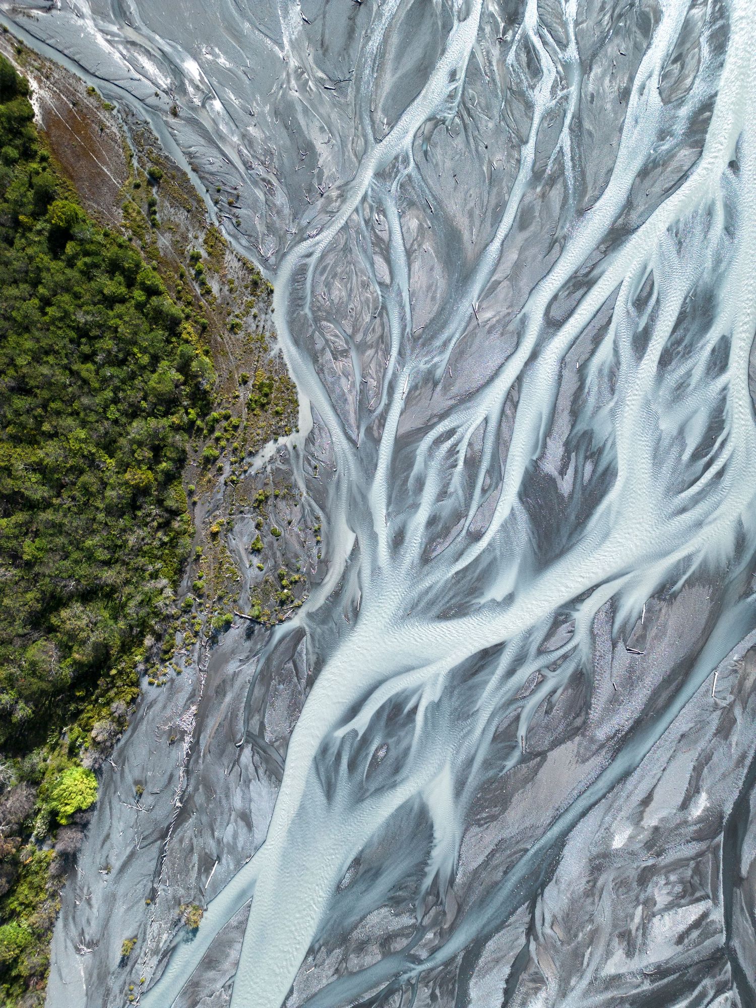 Aerial view of braided glacial river with blue-gray water channels weaving through rocky terrain.