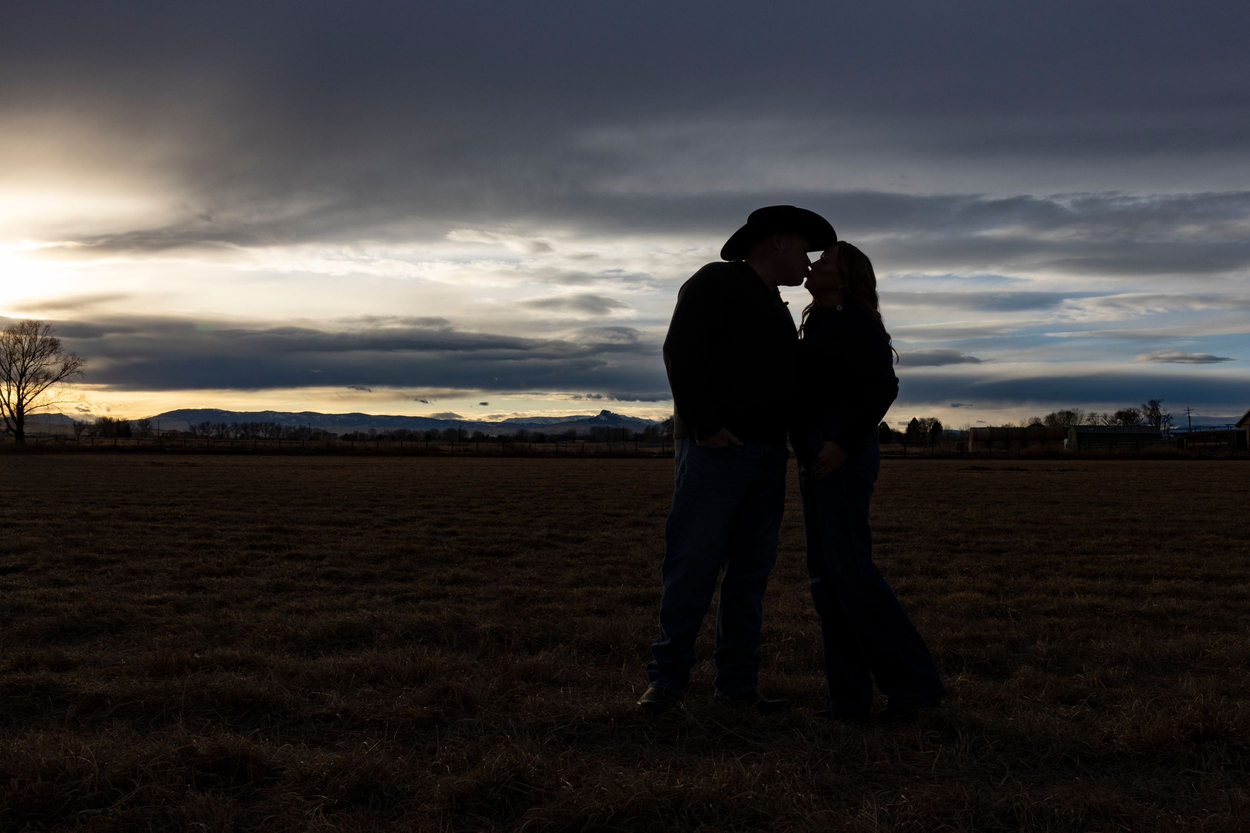Romantic silhouette of couple embracing at sunset in open field.