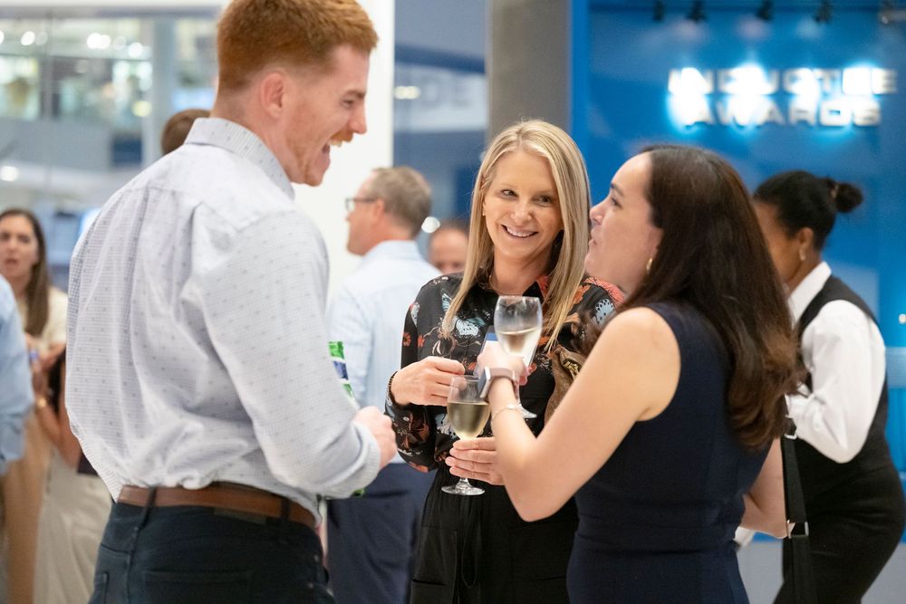 A group of professionals enjoying conversation and drinks at a networking event in a bright office space.