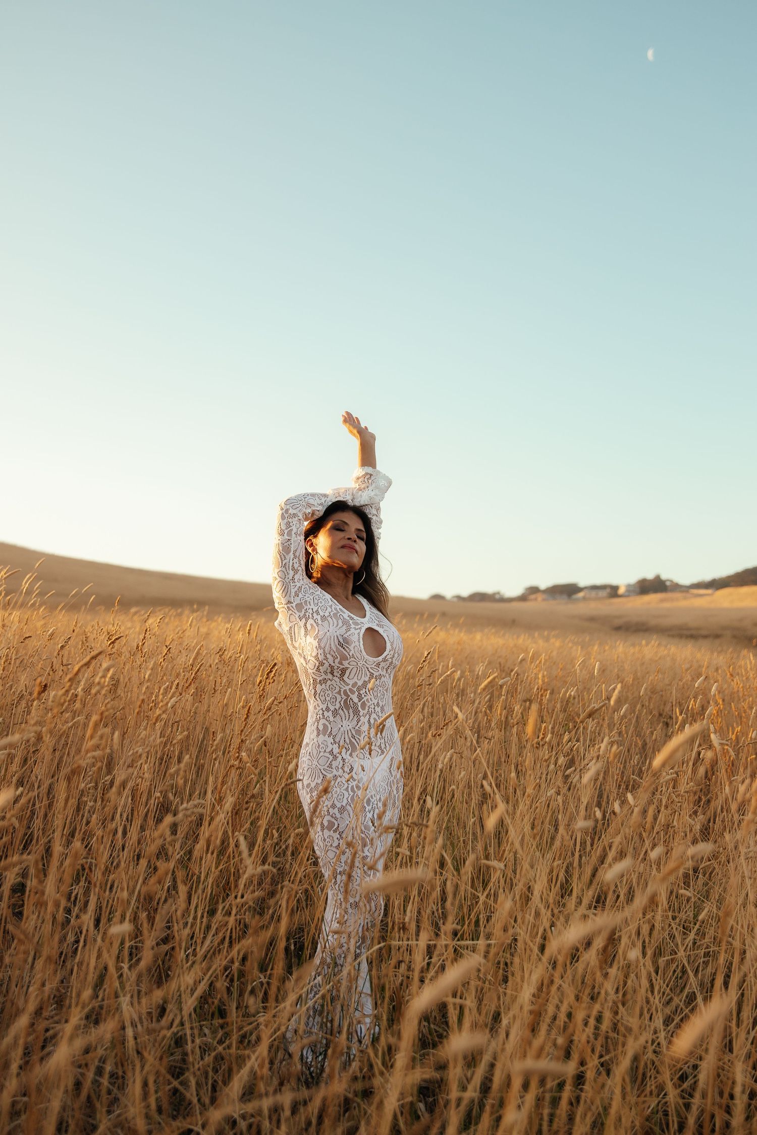 A figure in a white lace dress stands gracefully among golden wheat fields at sunset creating a dreamy atmosphere.