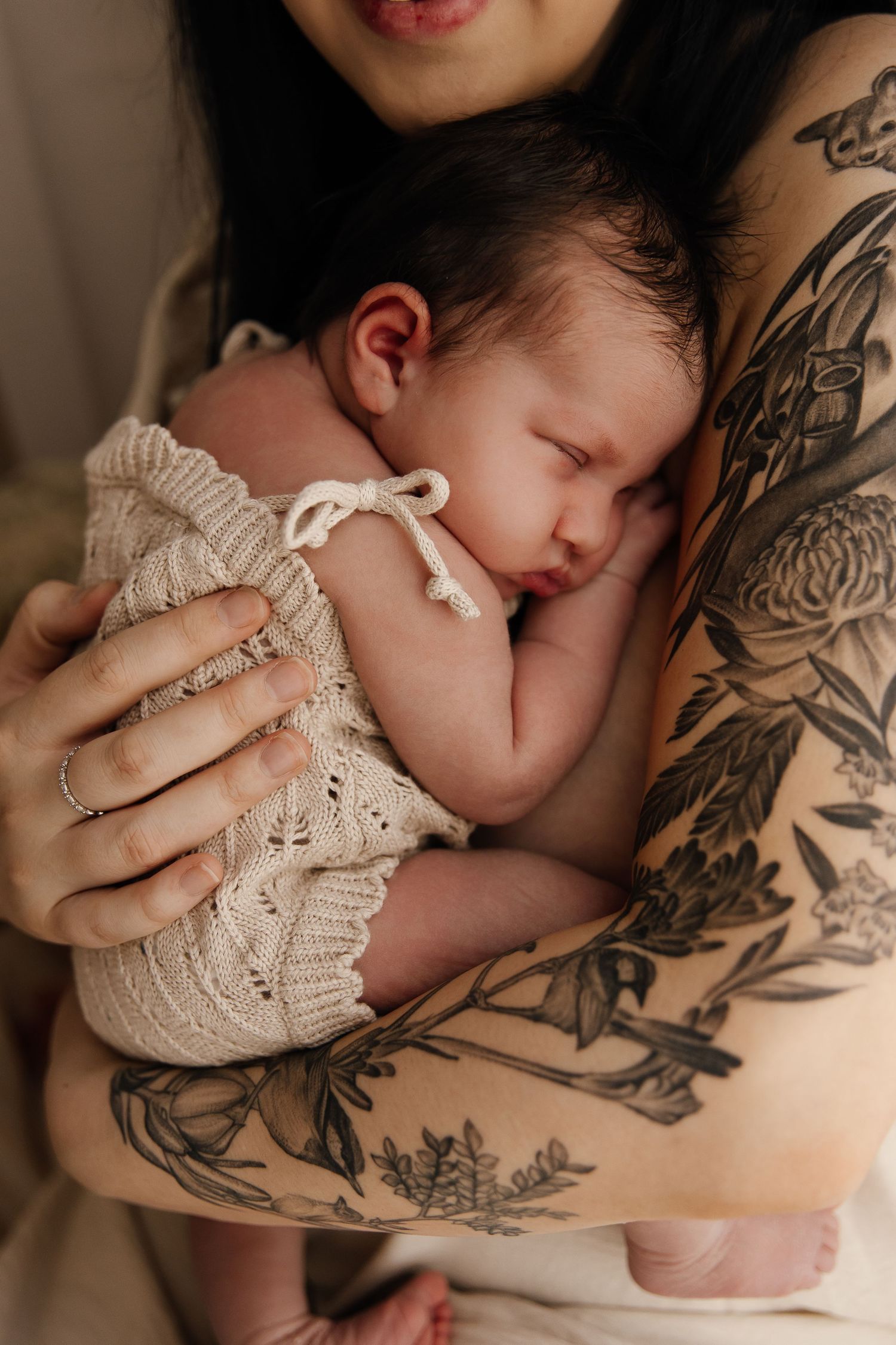 A sleeping newborn baby rests peacefully against a tattooed arm in a series of intimate black and white photographs.