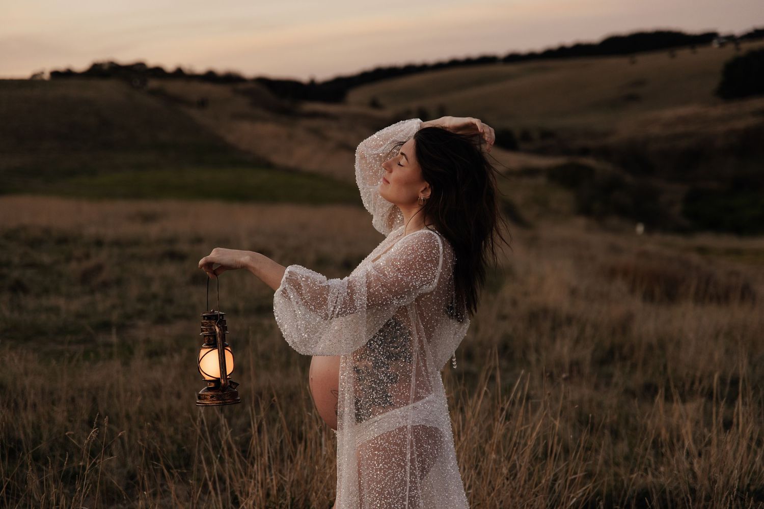 Maternity portrait at beach with golden sunlight streaming through white flowing dress.