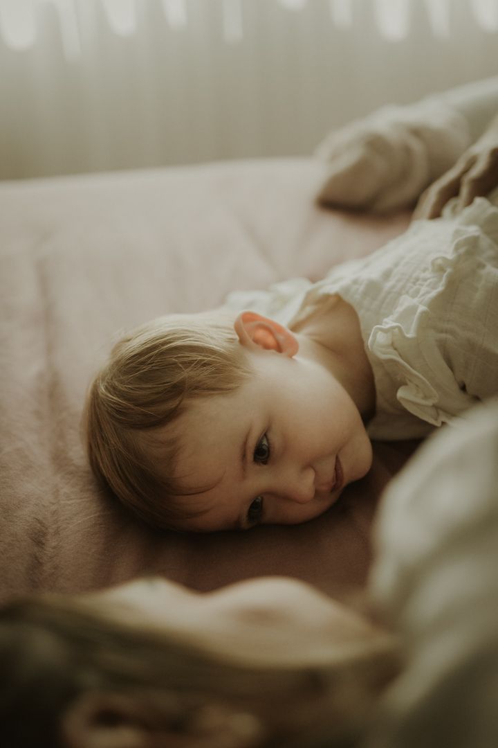 A dreamy closeup of a small child resting on soft bedding in muted lighting.