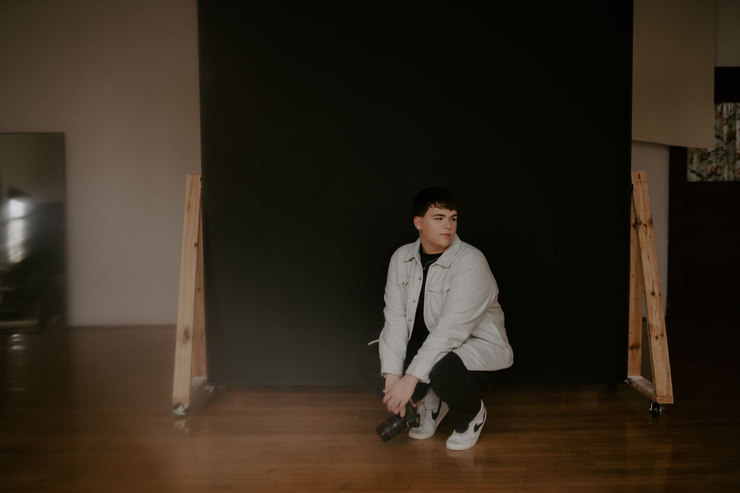 A person in a light jacket crouches on a wooden floor in a dark room.