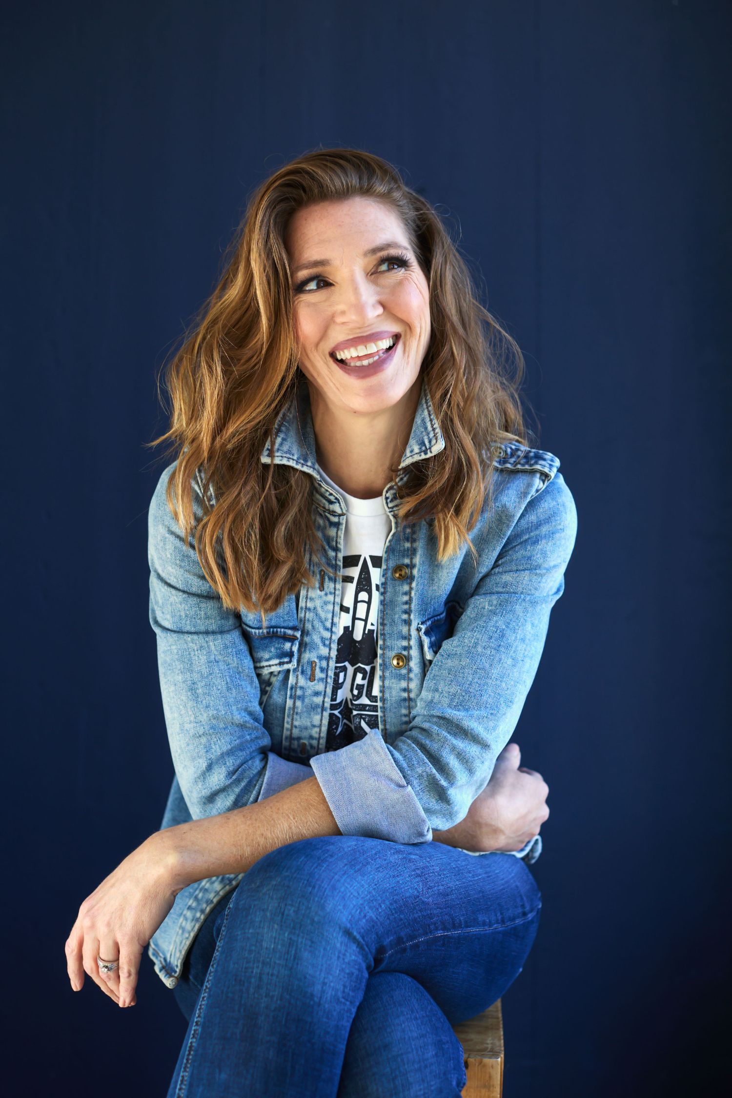 Professional studio portrait showing casual denim style against dark blue background.