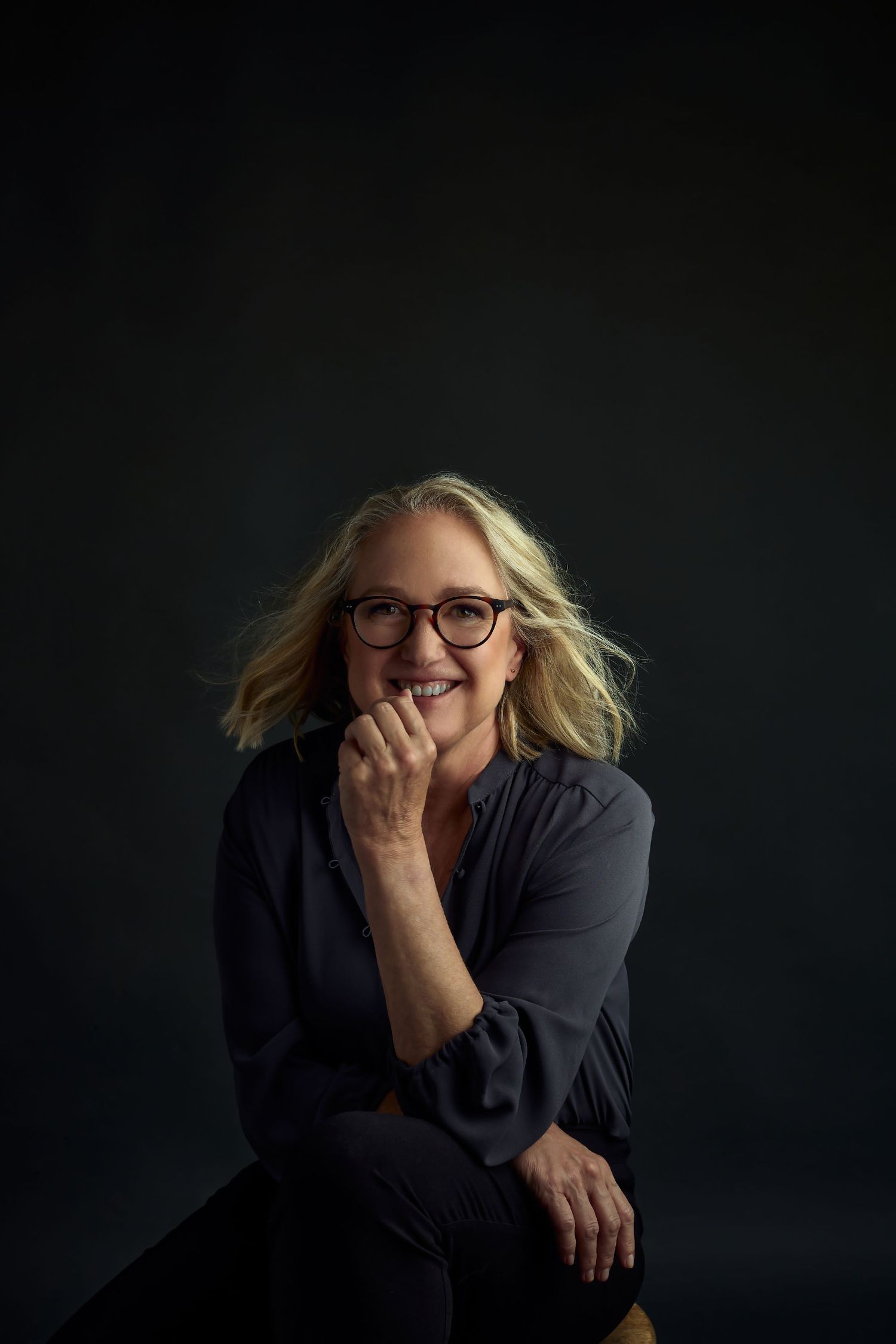 Artistic portrait with glasses in dark attire against black background.